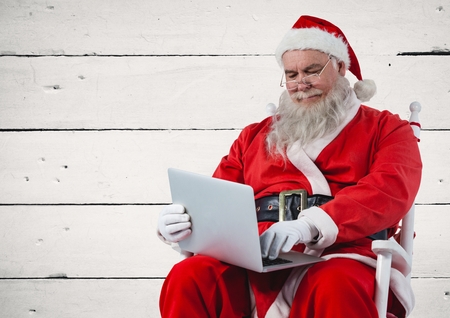 Santa sitting on chair and using laptop against wooden backgroundの写真素材