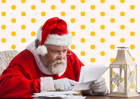Santa claus reading christmas wish letter against yellow polka dot backgroundの写真素材