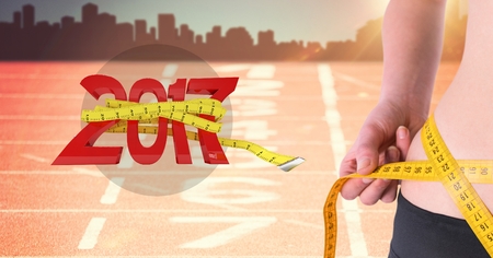 Mid section of woman measuring her waist against 2017 on running track