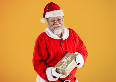 Portrait of santa claus holding gift box against yellow backgroundの写真素材