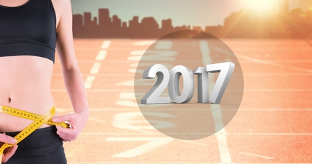 Mid section of woman measuring her waist against 2017 on running trackの写真素材