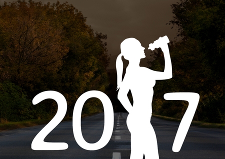 Silhouette of woman with sipper bottle forming 2017 new year sign against road in background