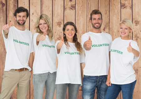 Portrait of group of volunteers showing thumbs up against wooden backgroundの写真素材