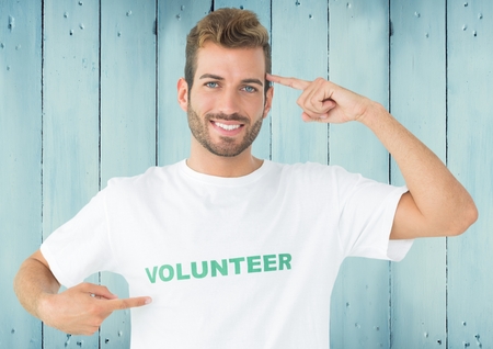 Portrait of smiling man in volunteer tshirt pointing at head against wooden backgroundの写真素材