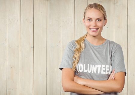 Portrait of confident female volunteer standing with arms crossed against wooden backgroundの写真素材