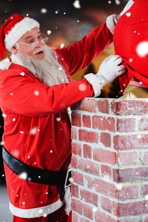 Santa claus placing gift box into a chimney against fir tree forest in snowy landscapeの写真素材