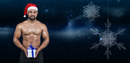 Muscular man in santa hat against snowflakes hanging against starry skyの写真素材