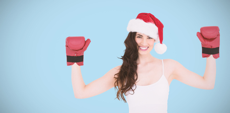 Festive brunette in boxing gloves with arms raised against blue backgroundの写真素材