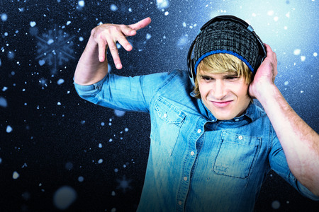 Cheerful hipster listening to music against snow with red flakes