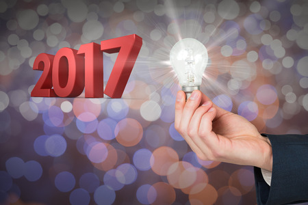 Hand holding light bulb against glowing backgroundの写真素材