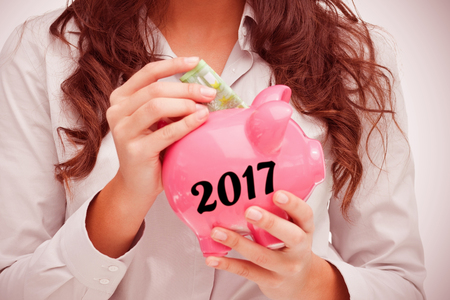 Brunette putting money in a piggy bank against digital image of new year 2017の写真素材