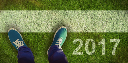 Man with canvas shoes on hardwood floor against closed up view of grass