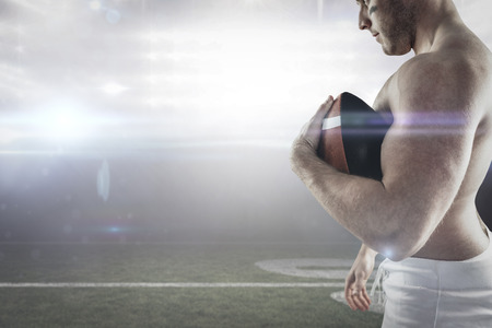 3D Shirtless American football player with ball against american football arenaの写真素材