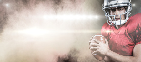 3D Portrait of serious American football player holding ball against splashing of color powderの写真素材