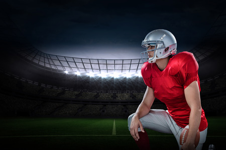 3D American football player looking away while kneeling against rugby stadiumの写真素材