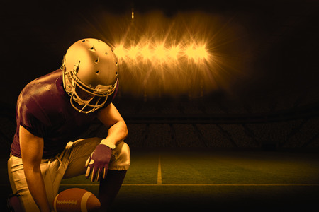 3D American football player kneeling while holding ball against rugby stadiumの写真素材