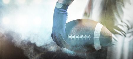 3D Cropped image of sportsman holding American football ball ball against digitally generated image of color powderの写真素材