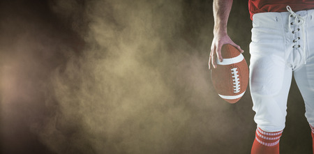 3D American football player holding up football against splashing of yellow color powderの写真素材
