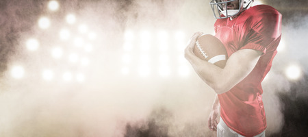3D Portrait of confident American football player in red jersey holding ball against splashing of color powderの写真素材
