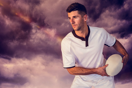 3D Rugby player focusing while holding ball against gloomy skyの写真素材