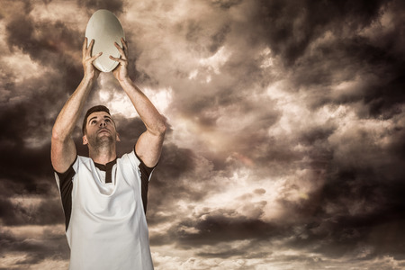 3D Rugby player holding rugby ball against gloomy skyの写真素材
