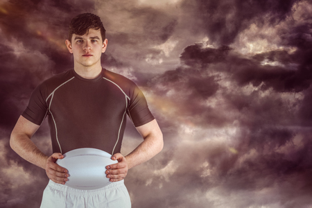 3D Rugby player holding a rugby ball against gloomy skyの写真素材