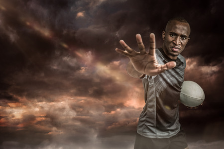 3D Close-up portrait of sportsman gesturing while standing with rugby ball against gloomy skyの写真素材