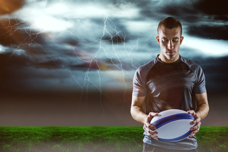 3D Serious rugby player holding ball against stormy dark sky with lightning boltsの写真素材