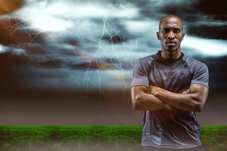 Portrait of athlete standing with arms crossed against stormy dark sky with lightning boltsの写真素材