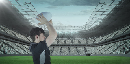 3D Profile view of rugby player throwing a ball against rugby stadiumの写真素材