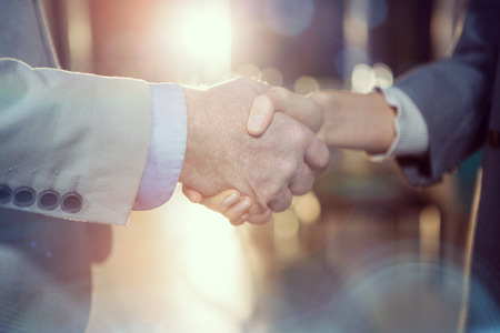 Close-up of businessman shaking hands with colleague in officeの写真素材