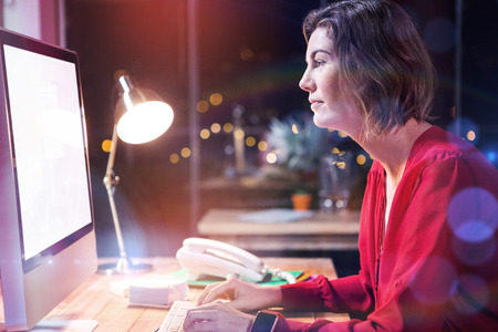 Businesswoman working on computer at desk while sitting in officeの写真素材