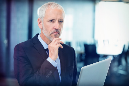 Thoughtful businessman thinking while working on laptop in officeの写真素材