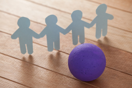Paper cut outs forming a human chain with a ball in front on wooden tableの写真素材