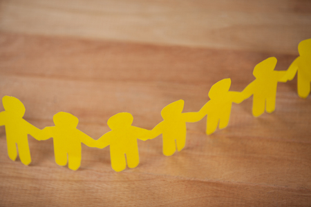 Close-up of paper cut outs forming a human chain on wooden tableの写真素材