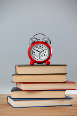 Alarm clock and stack of books on wooden tableの写真素材