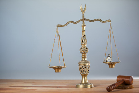 Conceptual image of watch and coins on the justice scale and a wooden hammer next to itの写真素材