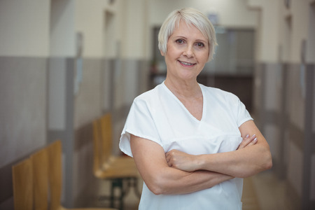 Portrait of female nurse standing with arms crossed in corridor at hospitalの写真素材