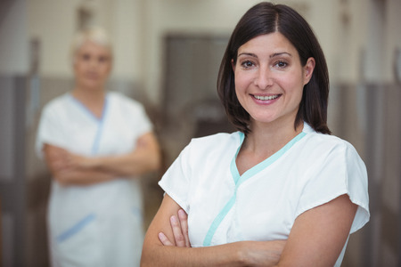 Portrait of female nurse standing with arms crossed in corridor at hospitalの写真素材