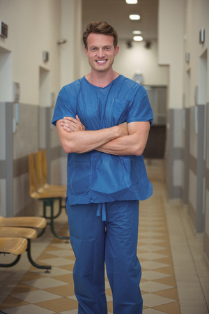 Portrait of male surgeon standing with arms crossed in corridorの写真素材