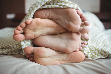 Couple showing their feet while lying on a bed in bedroomの写真素材
