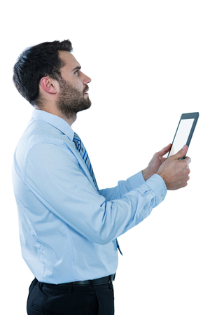 Businessman looking up while holding a digital tablet against white backgroundの写真素材