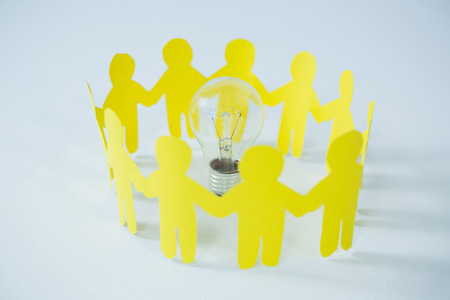 Circle of yellow paper cut-out figures and light bulb on white backgroundの写真素材