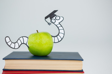 Conceptual image of books, apple and snake with graduate cap on white backgroundの写真素材