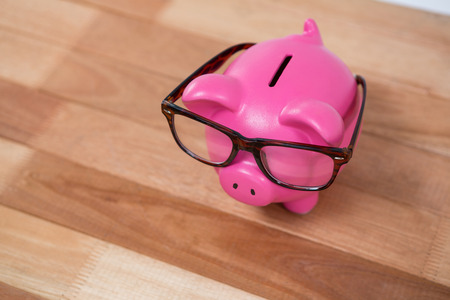 Close-up of pink piggy bank with spectacles on wooden tableの写真素材
