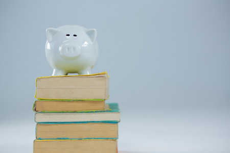 Piggy bank on stack of books against white backgroundの写真素材