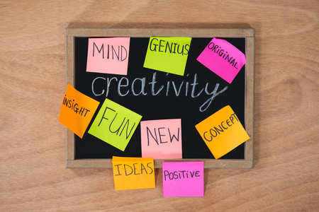 Close-up of sticky note stuck on slate board that reads creativityの写真素材