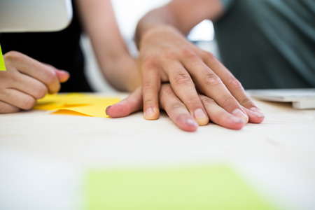Close-up of office colleagues with hand on hand at desk in officeの写真素材