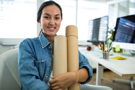 Portrait of woman sitting on a chair and holding chart holder in officeの写真素材