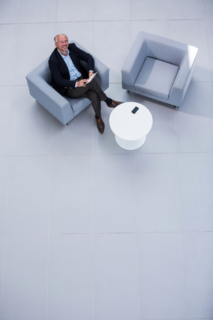Top view of businessman sitting on sofa with digital tablet and looking up in officeの写真素材